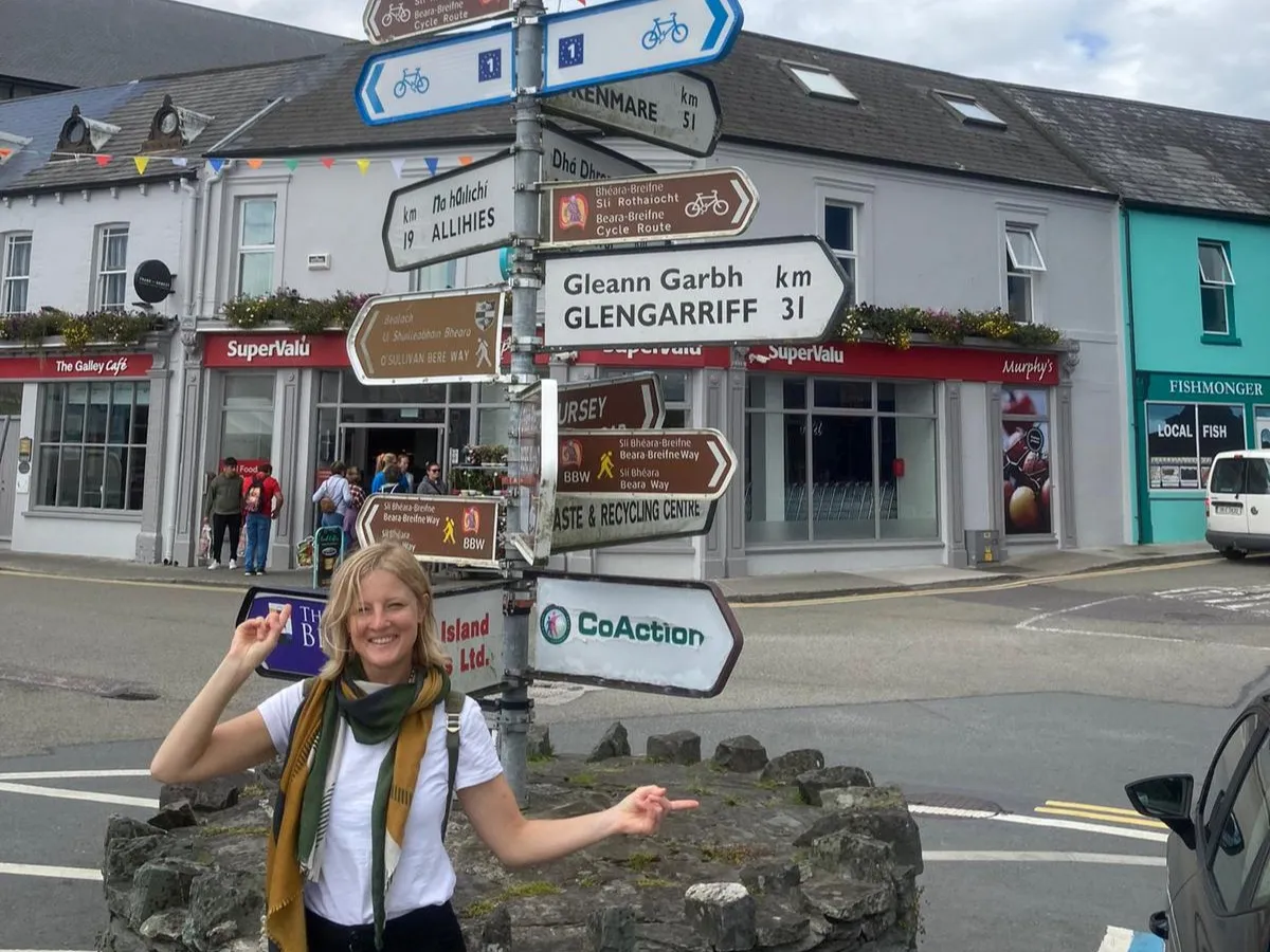 Lucy wears a white t-shirt, standing at a crossroads 
